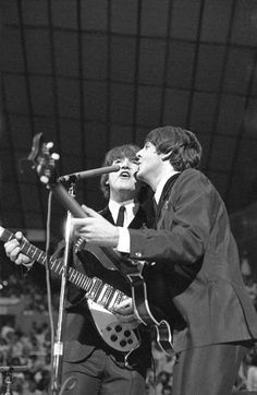 two young men singing into microphones while playing guitar in front of an audience at a concert