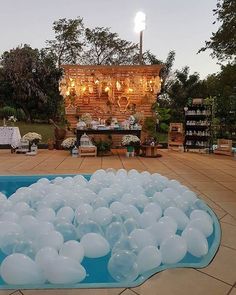 an outdoor wedding setup with balloons floating in the water at sunset or dusk, surrounded by tables and chairs