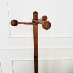 a wooden cross with three balls on the top and one at the bottom, in front of a white wall