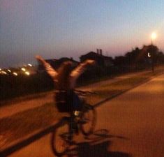 a person riding a bike down a street at night with their arms in the air