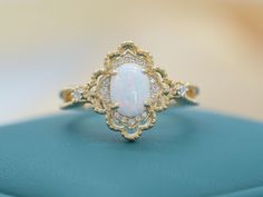 a white opal and diamond ring sitting on top of a blue box with gold trimming