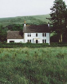 a white house sitting in the middle of a lush green field next to a forest