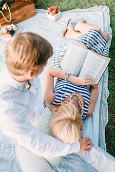 two people laying on a blanket reading books