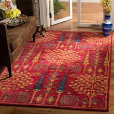 a red area rug with blue and yellow designs on the floor next to a couch