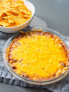 a cheesy dish with tortilla chips next to it on a table