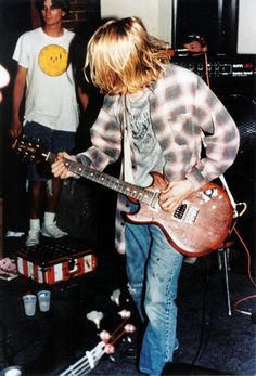 a young man playing an electric guitar in front of two other men standing behind him