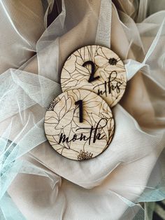 two wooden buttons with writing on them sitting on some white organine fabric and tulle