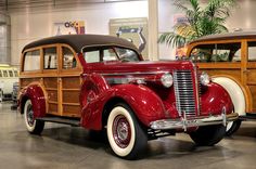 an old red car is parked in a building with other cars behind it and on display