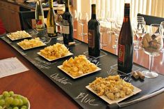 several plates of food and wine on a long table with bottles of wine in the background