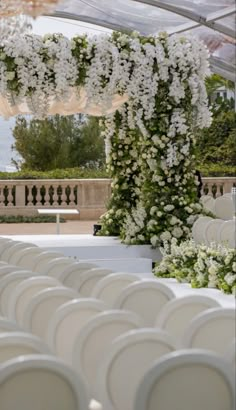 an outdoor wedding setup with white flowers and greenery on the back wall, along with rows of chairs