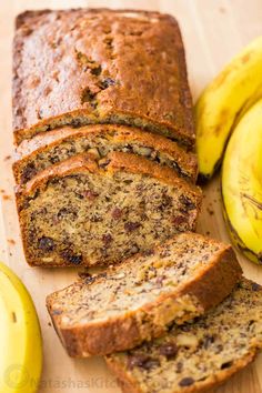 sliced banana bread on a cutting board next to two bananas