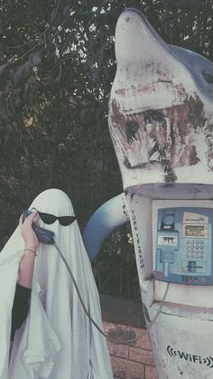 a person in a ghost costume standing next to a parking meter with a white sheet covering it's face