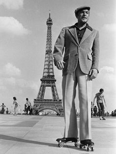 a man in a suit and hat riding a skateboard near the eiffel tower