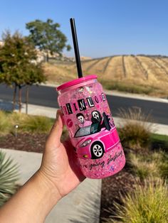 a person holding up a pink drink in front of a road with hills and trees