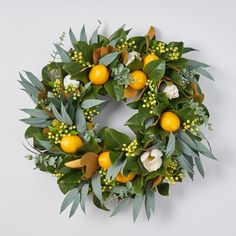 a wreath with oranges and green leaves on a white background, surrounded by greenery