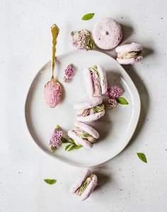 a white plate topped with donuts covered in pink frosting and green leafy toppings