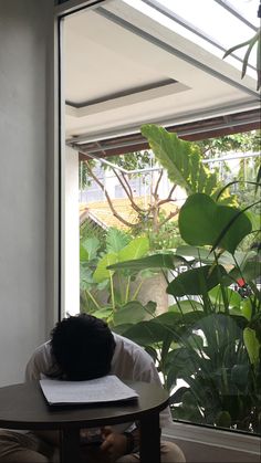 a person sitting at a table in front of a window looking out onto the garden