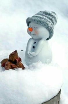 a snowman sitting in the snow next to a tree stump with his eyes closed