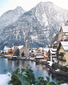 a snowy town with mountains in the background and snow on the ground, along side water