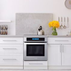 a modern kitchen with white cabinets and stainless steel appliances, yellow flowers in vases on the counter