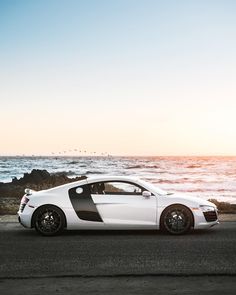 a white and black sports car parked on the side of the road next to the ocean