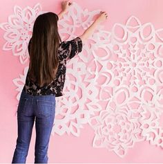 a woman is working on an intricate paper wall decoration with white flowers and leaves, against a pink background