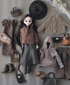 an assortment of doll clothes and accessories are laid out on a gray surface next to a black purse