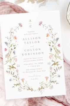 the wedding stationery is laid out on top of a pink blanket with flowers and leaves