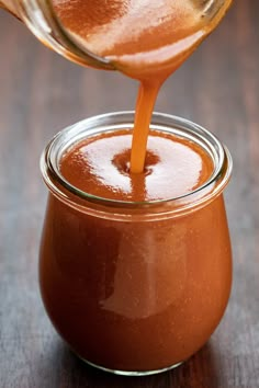 someone pouring caramel sauce into a glass jar