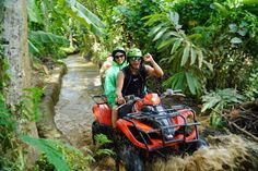 two people riding atvs through the jungle