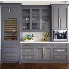 a kitchen with gray cabinets and marble counter tops, along with wine glasses on the glass doors