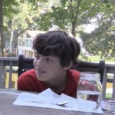 a young boy sitting at a table with food and water in front of his face