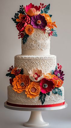 a three tiered wedding cake decorated with colorful flowers and lace on a white pedestal