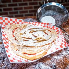 a stack of pancakes on top of a red and white checkered plate next to a frying pan