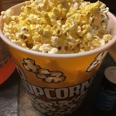 a bucket filled with popcorn sitting on top of a table next to a bottle of soda