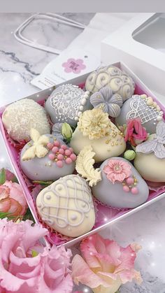 a pink box filled with lots of different types of chocolates next to some flowers