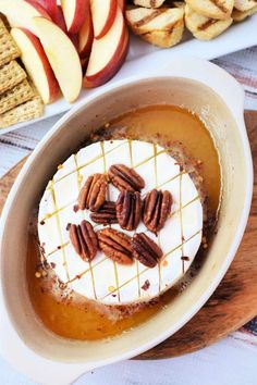 a dessert in a bowl with pecans on top and apples around the bowl, along with crackers