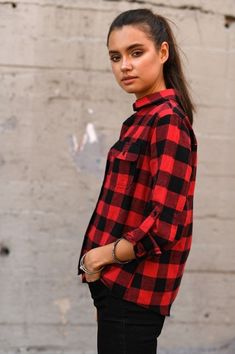 a woman standing in front of a wall wearing a red and black checkered shirt