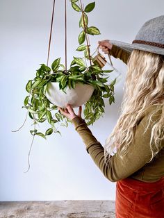 a woman is holding a potted plant in her right hand while wearing a hat