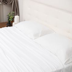 a bed with white sheets and pillows on top of it next to a vase filled with flowers