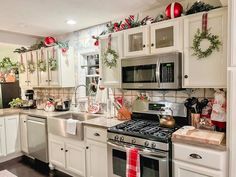 a kitchen decorated for christmas with white cabinets, silver appliances and wreaths on the wall