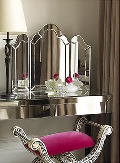 a mirror sitting on top of a table next to a pink chair and a lamp