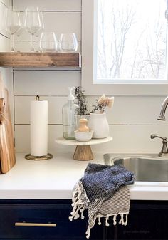 a kitchen sink and counter with wine glasses on the shelf above it, next to a window