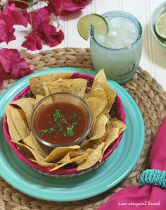 a plate with chips and salsa on it next to a glass of water, lime wedges and flowers