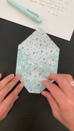 two hands are holding an origami hexagonal object on top of a table