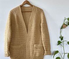 a cardigan sweater hanging on a wall next to a potted plant and a wooden hanger