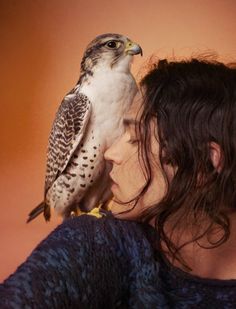 a woman is holding a bird on her shoulder while she looks at it's face