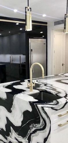 a kitchen with black and white marble countertops, gold accents and pendant lights hanging from the ceiling