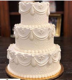 a three tiered white wedding cake sitting on top of a wooden table