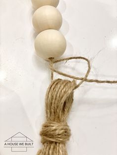 three wooden beads are tied to twine on a white surface with a house in the background